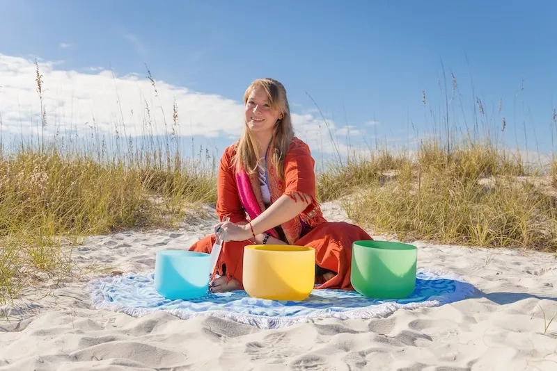 Aarika on the beach using her singing bowls for a sound bath